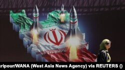 Ирандык аял Тегерандагы Израилге каршы маанайдагы жарнактын жанынан өтүп баратат. 19-апрель, 2024-жыл.
