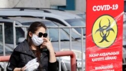 Женщина в маске рядом с баннером, предупреждающим об опасности COVID-19 и призывающим носить маски.